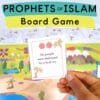 Hand holding a Prophets Game card that reads “His people were destroyed by a loud cry,” with colorful board and more question cards in the background. Text overlay reads “Prophets of Islam Board Game.”